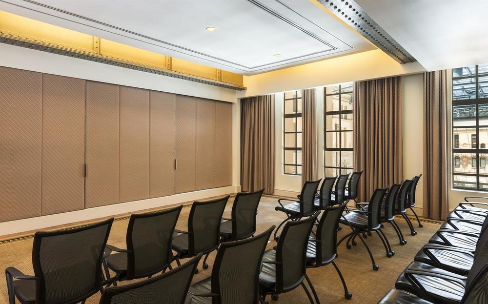 The Fullerton Hotel Sydney Exterior foto The photo shows a modern conference room or meeting space. There are several rows of black chairs arranged facing a wall. The walls appear to have a beige tone with large windows adorned with curtains, allowing natural light to enter. The ceiling is 
