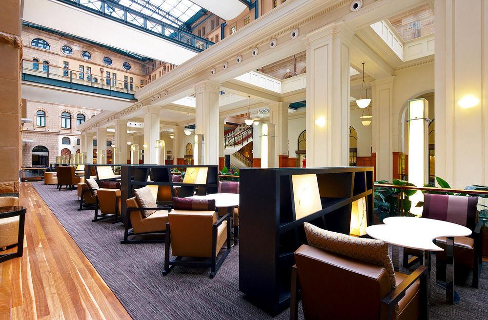The Fullerton Hotel Sydney Exterior foto The photo features a spacious and well-lit interior of a lounge or café area, characterized by high ceilings and large windows that allow natural light to flood the space. The design includes elegant architectural details, such as tall columns and an