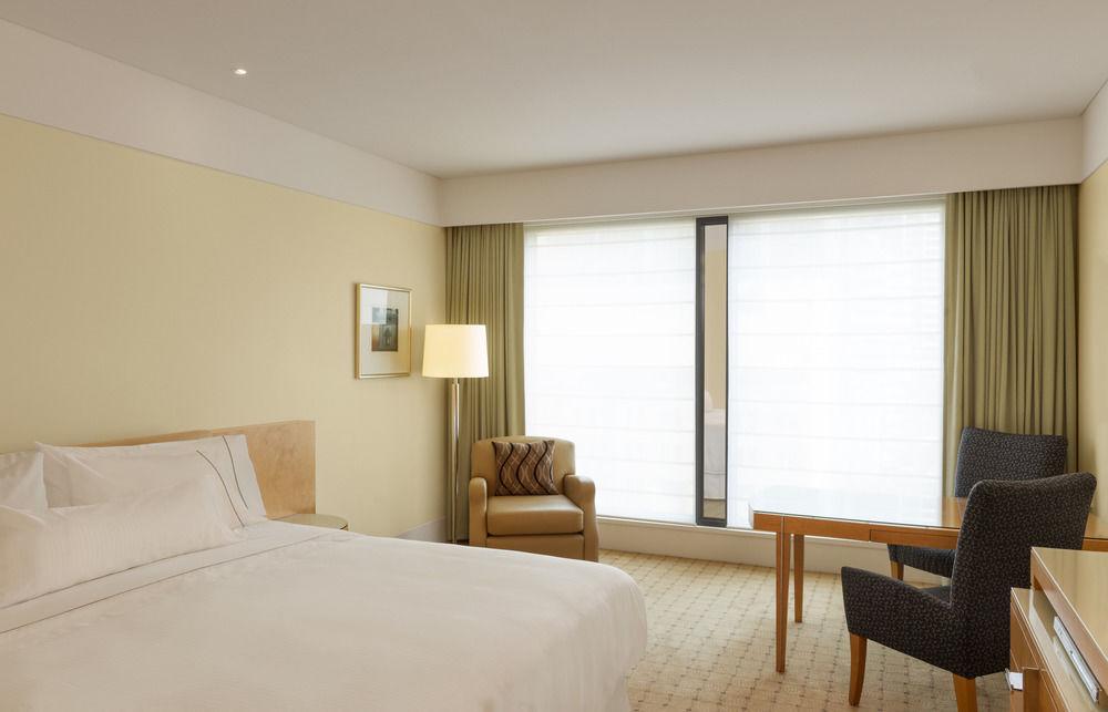 The Fullerton Hotel Sydney Exterior foto The photo shows a modern hotel room. The decor features soft, neutral colors, creating a calm and inviting atmosphere. There is a large bed with crisp white linens against one wall. A bedside lamp stands on a small table next to the bed. 

Near the w