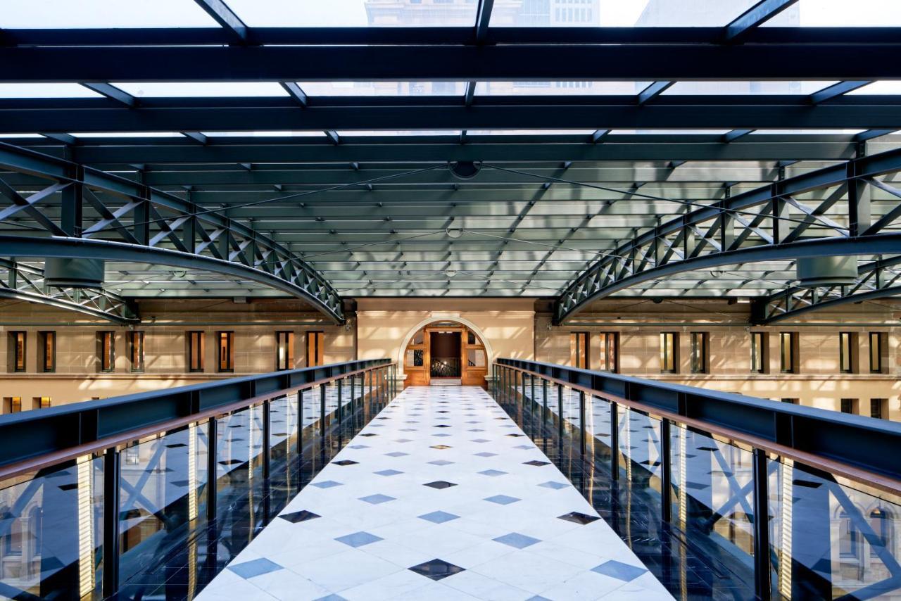 The Fullerton Hotel Sydney Exterior foto The photo shows an interior space featuring a modern architectural design. There is a wide corridor or walkway made of patterned tiles, with a series of geometric shapes visible on the floor. Above, a glass ceiling allows natural light to flood the a