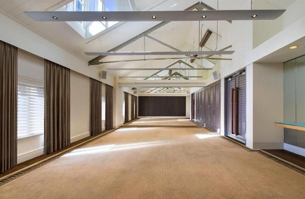 The Fullerton Hotel Sydney Exterior foto The photo depicts a spacious interior room with a high ceiling featuring exposed beams. The flooring appears to be carpeted in a neutral color. Natural light floods the room through large windows and skylights, creating a bright atmosphere. On the si