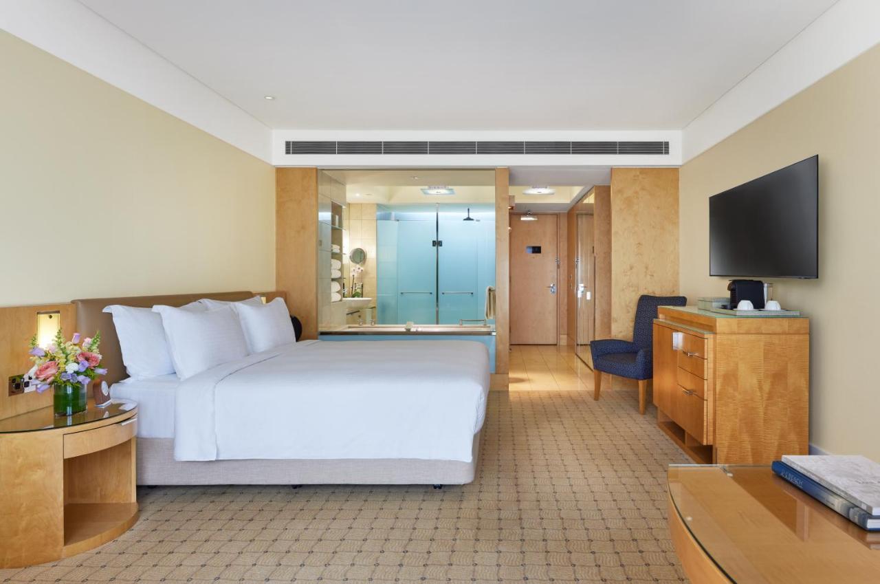 The Fullerton Hotel Sydney Exterior foto The photo depicts a modern hotel room featuring two neatly made beds with white linens. The room has light-colored walls and a warm, inviting atmosphere. On one side, there is a wooden bedside table, and a bouquet of flowers adds a touch of color. A 