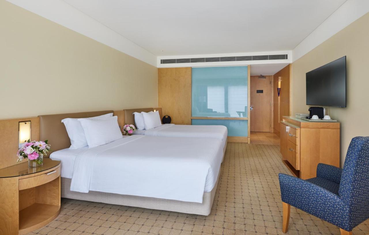 The Fullerton Hotel Sydney Exterior foto The image shows a hotel room featuring two twin beds with white linens and decorative pillows. The walls are painted in a soft beige color, and there is wooden furniture, including a bedside table and a media console. A flat-screen TV is mounted on t
