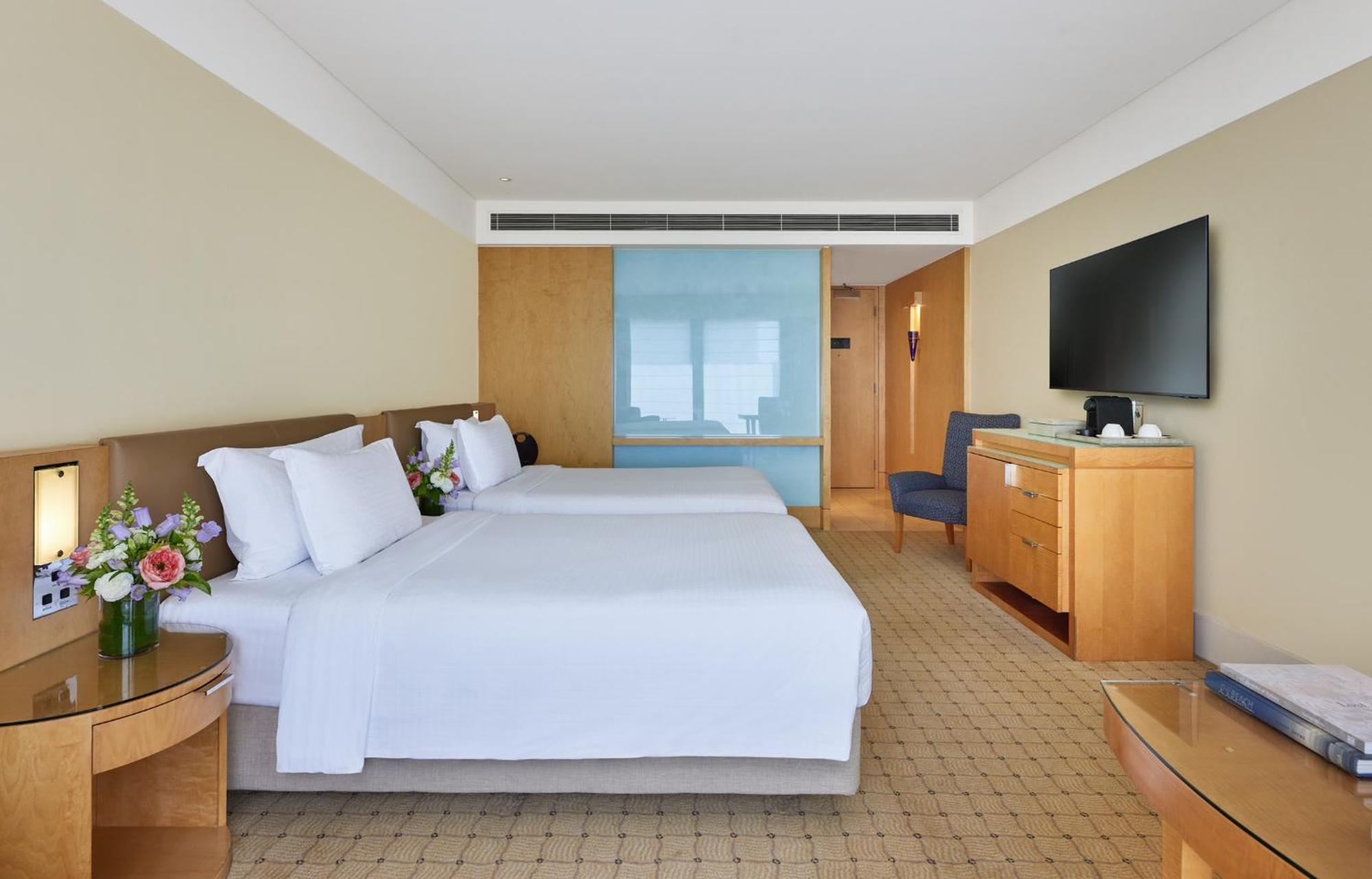 The Fullerton Hotel Sydney Exterior foto The photo shows a hotel room with two beds, each made up with white linens and pillows. There are small flower arrangements on the side tables next to the beds. The room has a light color scheme with beige walls and wooden furniture. A blue glass par