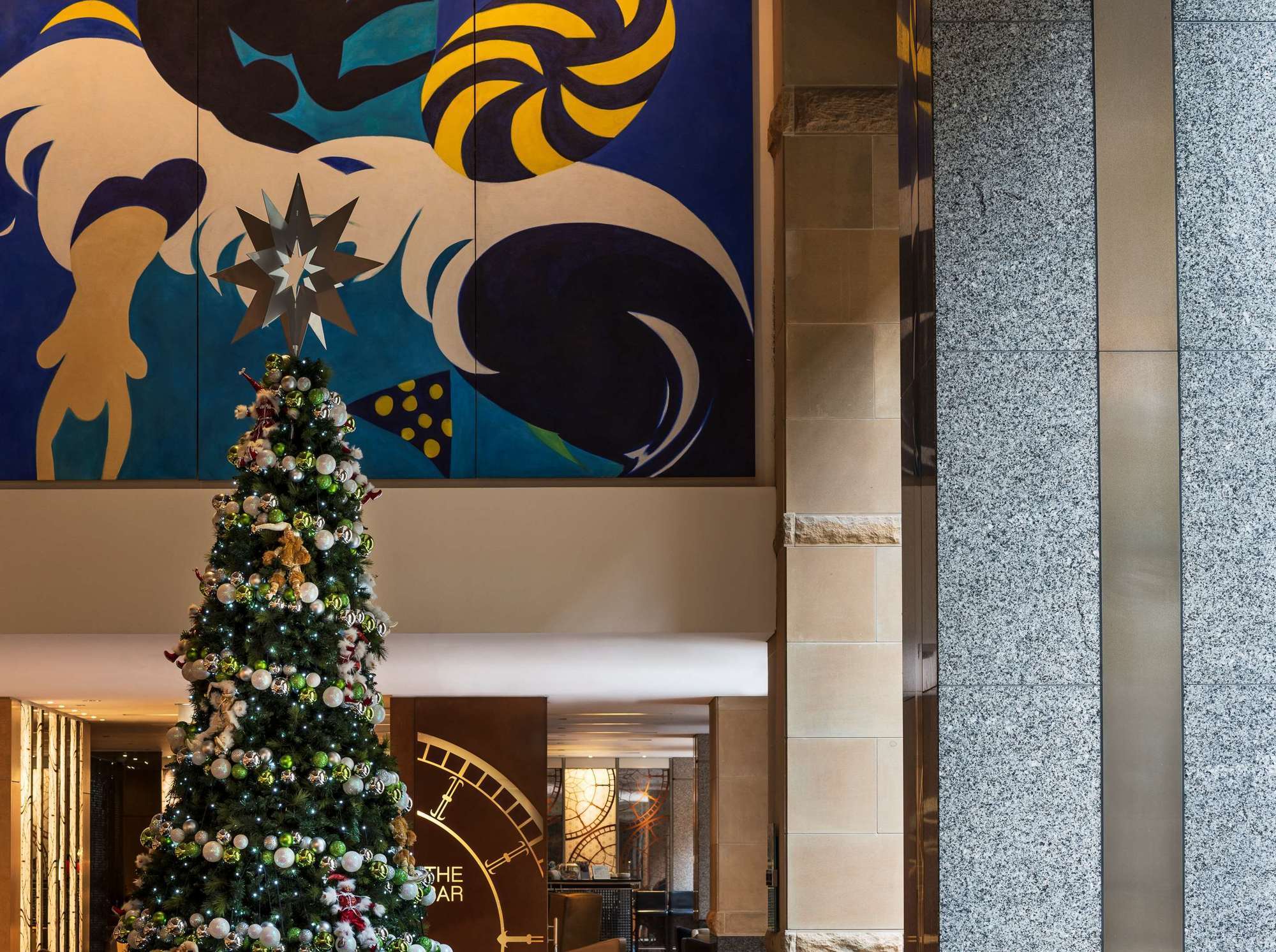 The Fullerton Hotel Sydney Exterior foto The photo shows a bright and modern lobby area. In the foreground, there is a beautifully decorated Christmas tree, adorned with ornaments and lights. Behind the tree, there is a large and colorful mural featuring abstract shapes and vibrant colors. 