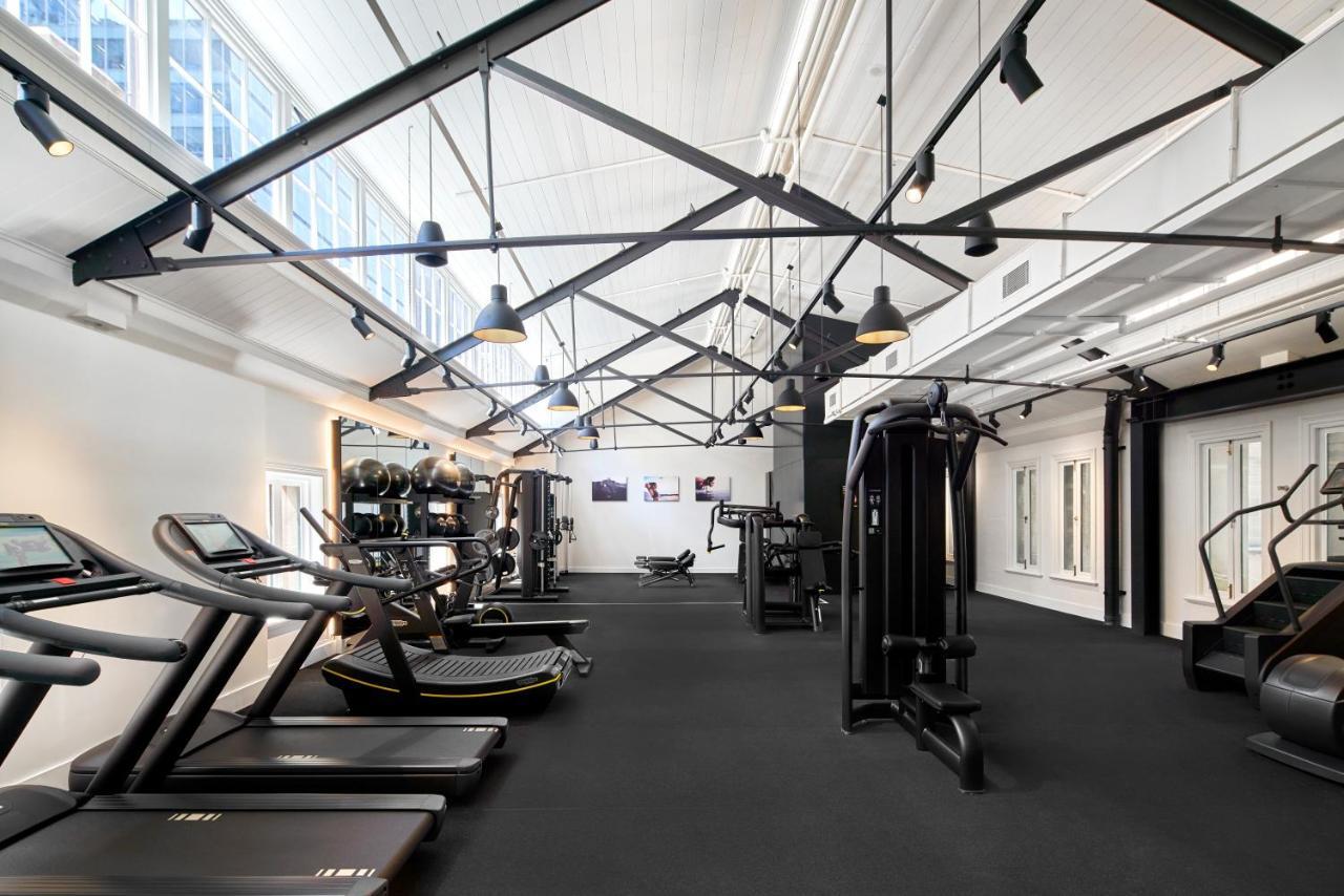 The Fullerton Hotel Sydney Exterior foto The photo shows a modern gym interior with various exercise equipment. There are treadmills that line one side and strength training machines on the other. The gym features a high ceiling with exposed beams and large windows that bring in natural lig