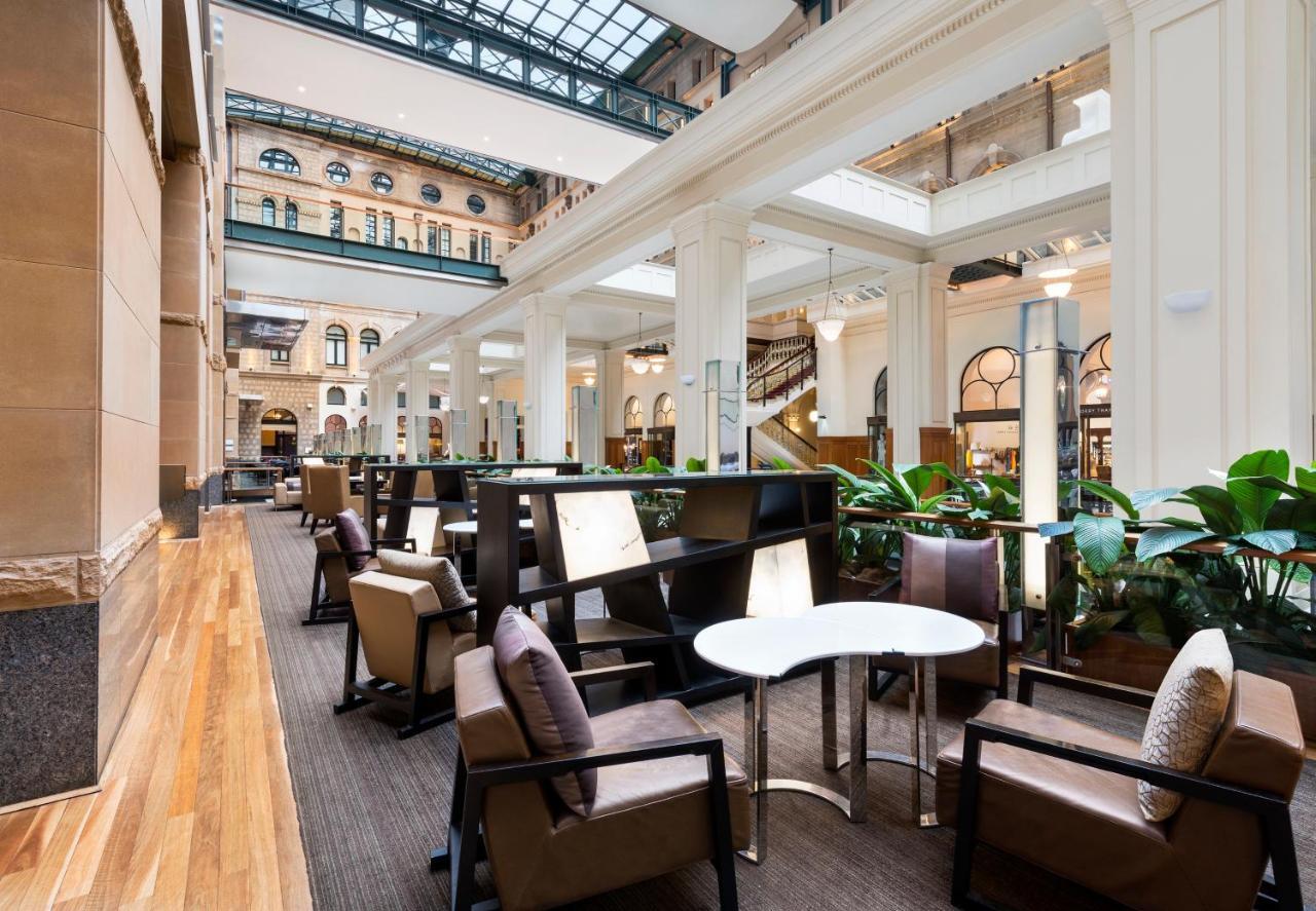 The Fullerton Hotel Sydney Exterior foto The photo depicts a stylish, modern interior space, likely a hotel lobby or lounge area. It features tall ceilings with large windows that allow plenty of natural light to enter. The flooring is a combination of wood and carpet, creating a warm atmos